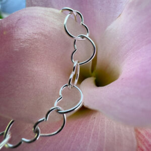 Close up of identical sterling silver hearts linked together to form a delicate ankle chain, displayed on a pink flower