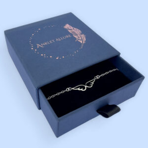 Cute silver anklet with an angel's wings sitting in the chain, presented in a blue jewellery box with Anklet Allure written on the top in rose gold.