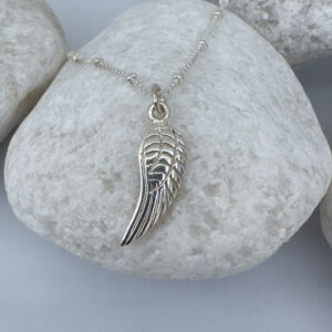 Silver anklet with a single angel wing pendant on a white rock.