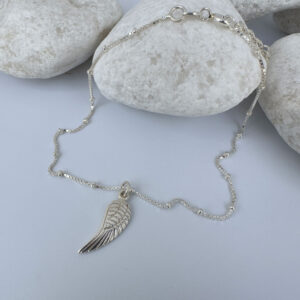 Silver anklet with a single angel wing pendant on white rocks.