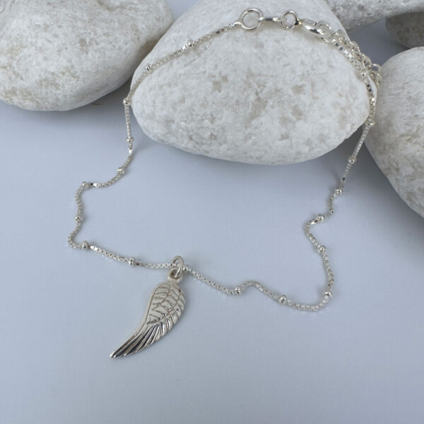 Silver anklet with a single angel wing pendant on white rocks.