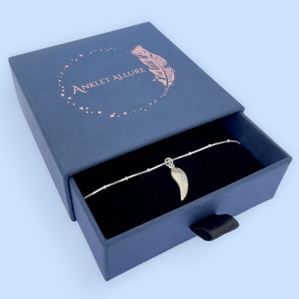Silver anklet with a single angel wing pendant, presented in a blue jewellery box with Anklet Allure written on the top in rose gold.