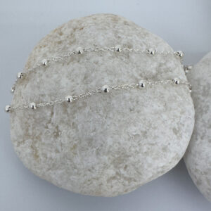 Cute silver anklet with small balls all the way around on a white rock.