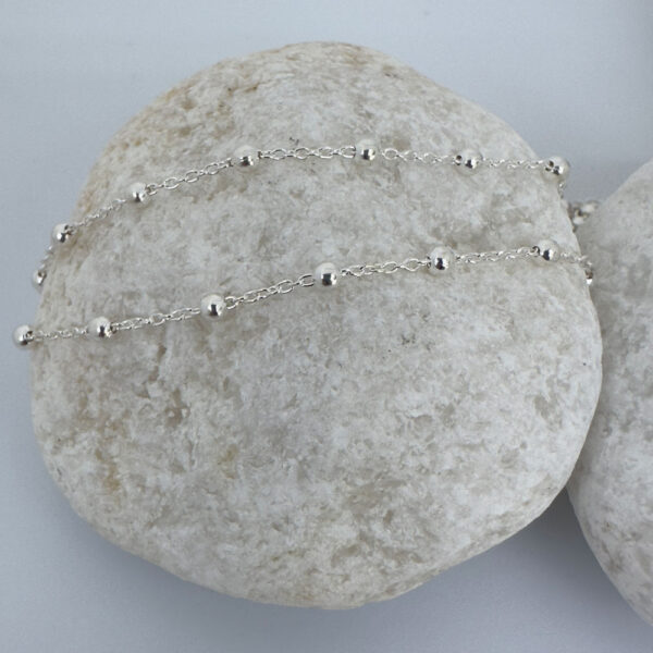 Cute silver anklet with small balls all the way around on a white rock.