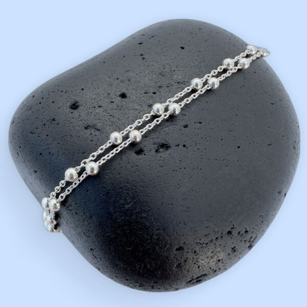 Pretty ankle bracelet in silver with small balls all the way around, on a black rock.