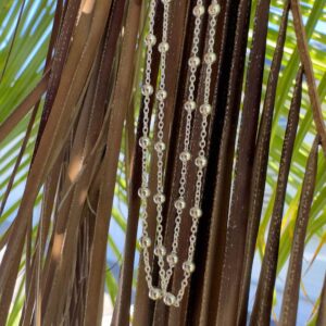 Sterling silver anklet with dainty silver balls attached all around the silver chain at equal distances and displayed hanging from a shaded tree with blue sky behind.