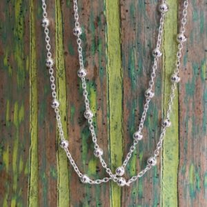 Silver ankle bracelet with small silver balls around the chain at equal distance, on a wooden background with green painted stripes.