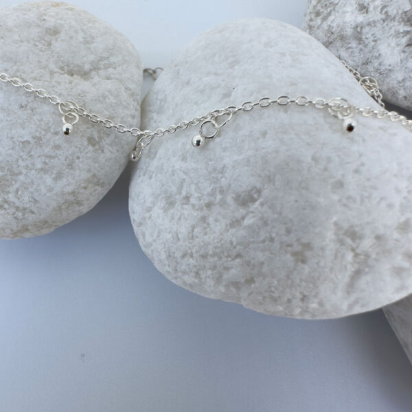 Dainty and gracious ankle bracelet with two hoops and a ball charms all the way around on white rocks.