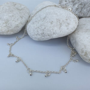 Dainty and gracious ankle bracelet with two hoops and a ball charms all the way around on white rocks.