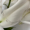 A gracious looking anklet with lots of small sterling silver balls hanging from it, equally spaced all the way around a dainty ankle chain, presented on a white lily petal.