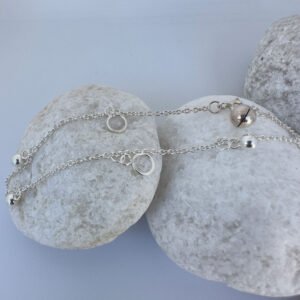 Beautiful silver anklet with hoop and ball charms equally spaced around on a white rock.
