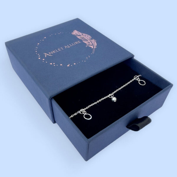 Beautiful silver anklet with hoop and ball charms equally spaced around, presented in a blue jewellery box with Anklet Allure written on the top in rose gold.