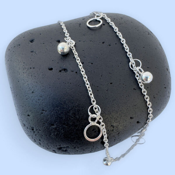 Beautiful silver anklet with hoop and ball charms equally spaced around, on a black rock.