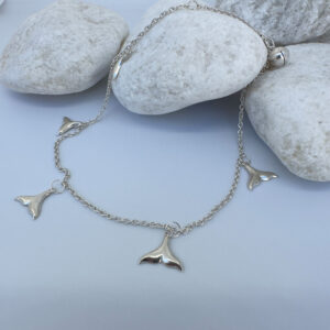 Anklet in silver with whale tail charms equally spaced around presented on white rocks.