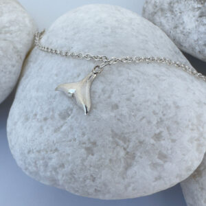 Anklet in silver with whale tail charms equally spaced around presented on a white rock.