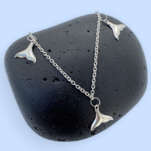 Anklet in silver with whale tail charms equally spaced around presented on a black rock.