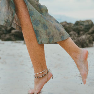 Legs of a lady walking in the beach wearing petite anklets.