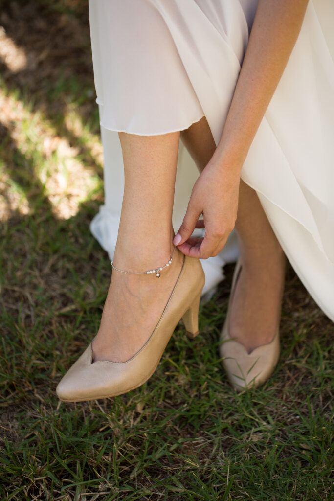 Bride in a white dress doing up a bridal anklet.